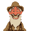 an old, gaunt man dressed as a gold prospector. he has a full, unkempt beard, a weathered face, and a broad smile revealing many missing teeth.